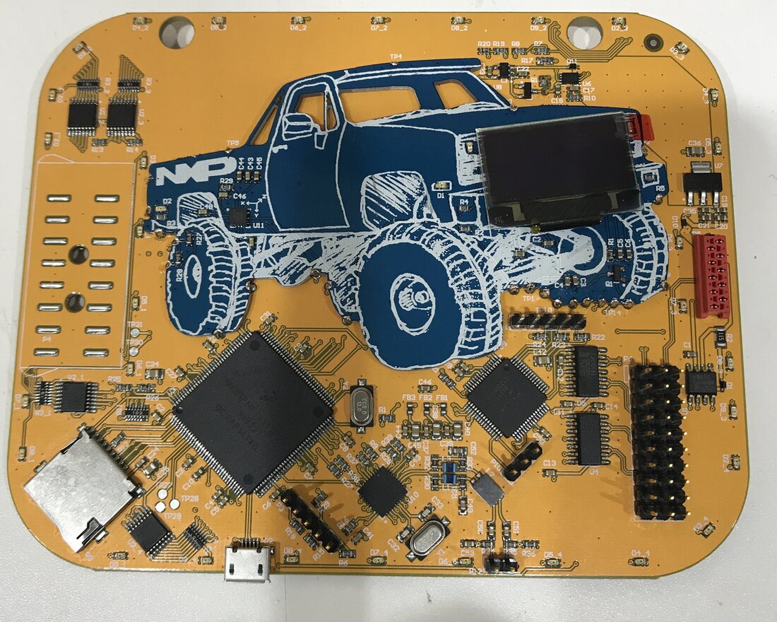 Assembled orange 2017 badge circuit board with a blue truck illustration, an OLED display, a microSD slot, micro-USB and several ICs