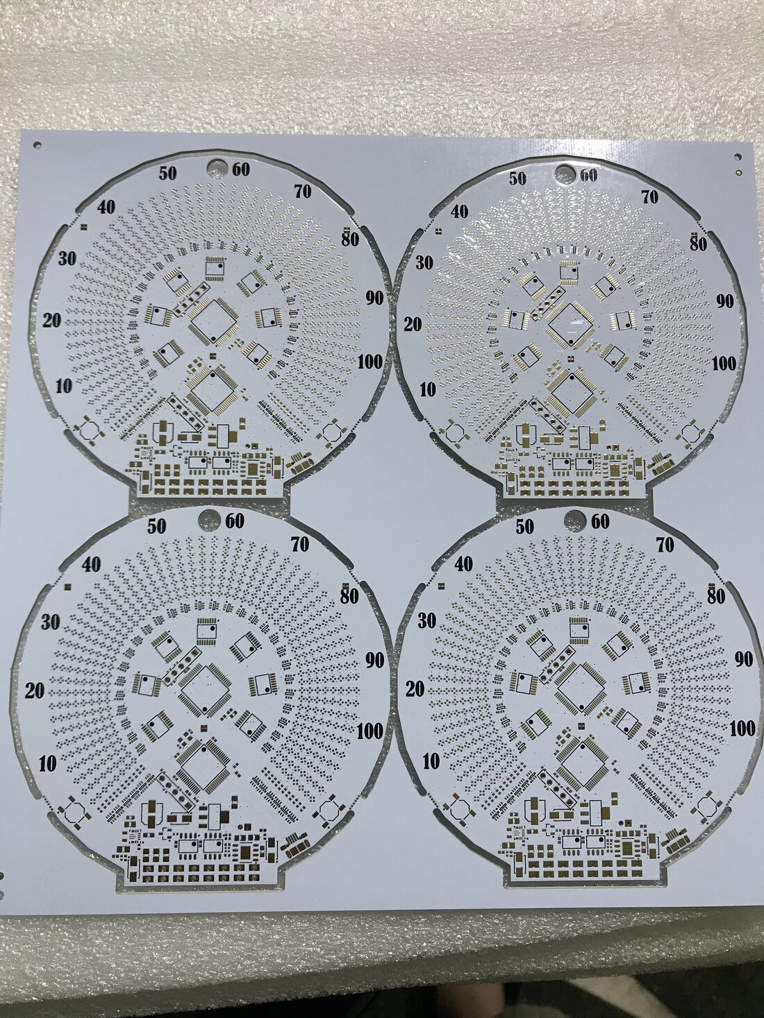 Panel of four bare white speedometer PCBs with the numbers 10 to 100 printed around the dial